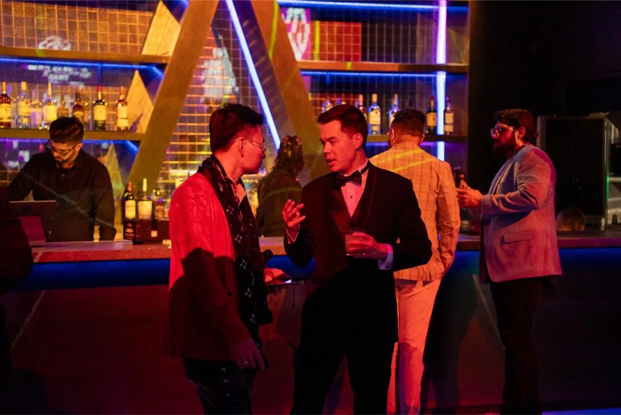 Guests in evening wear talking at the neon lit bar at Bad After Dark in Las Vegas