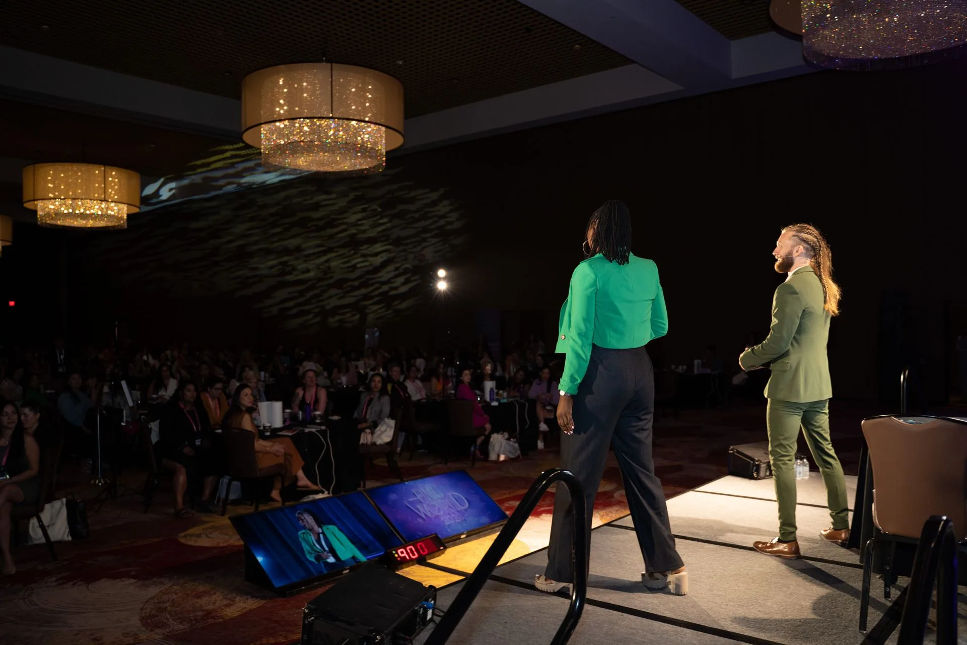 Two speakers on the main stage facing a packed, darkened ballroom at PMU World 2023, the Seminole Hard Rock Hotel & Casino in Hollywood, Florida