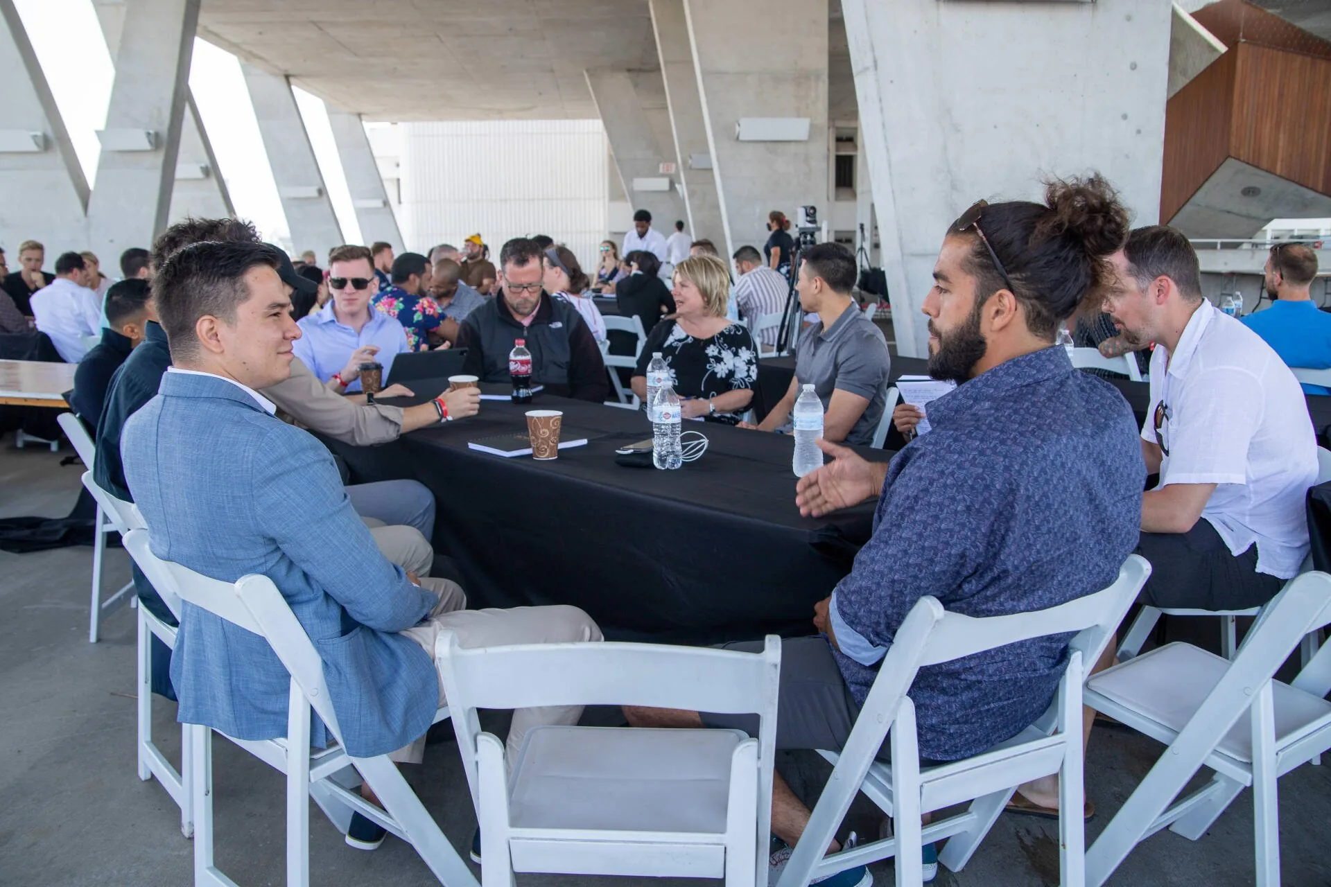 Attendees at round tables filling an open air concrete venue at Scaling With Systems LIVE in Miami