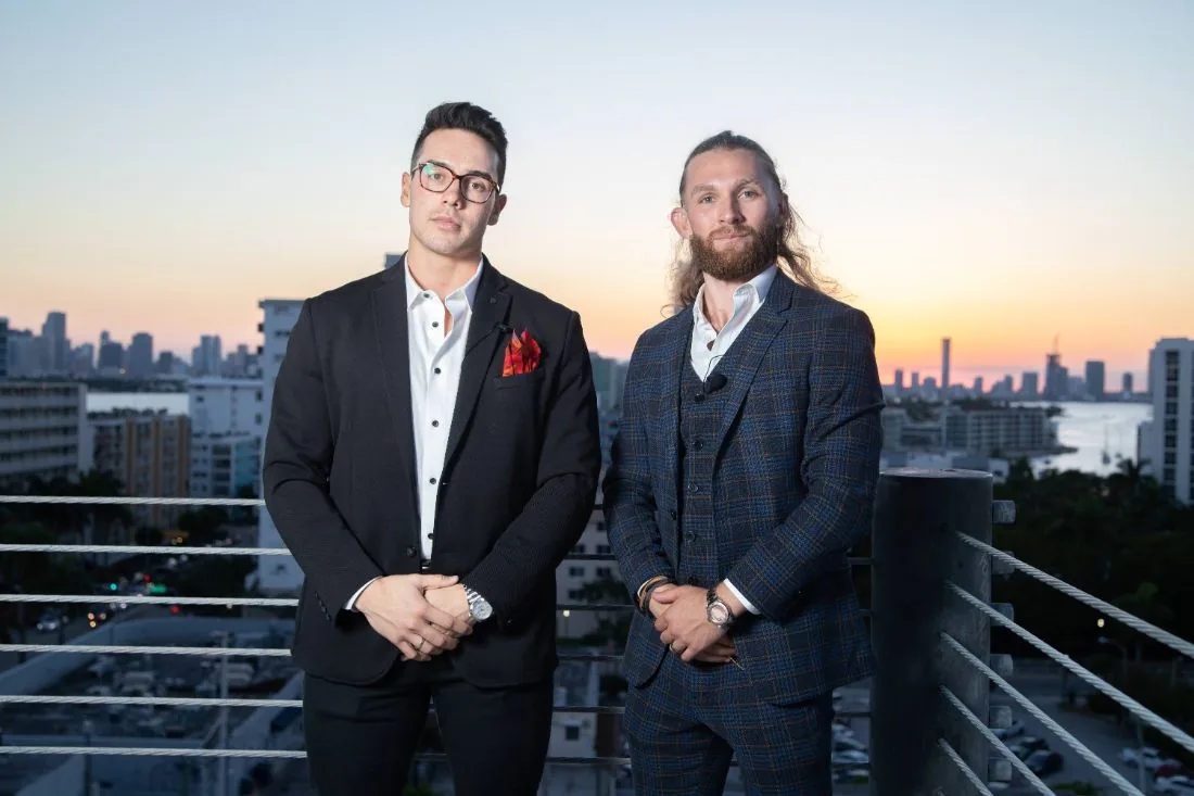 Two hosts in suits on a rooftop at sunset over the Miami skyline during Scaling With Systems LIVE in Miami