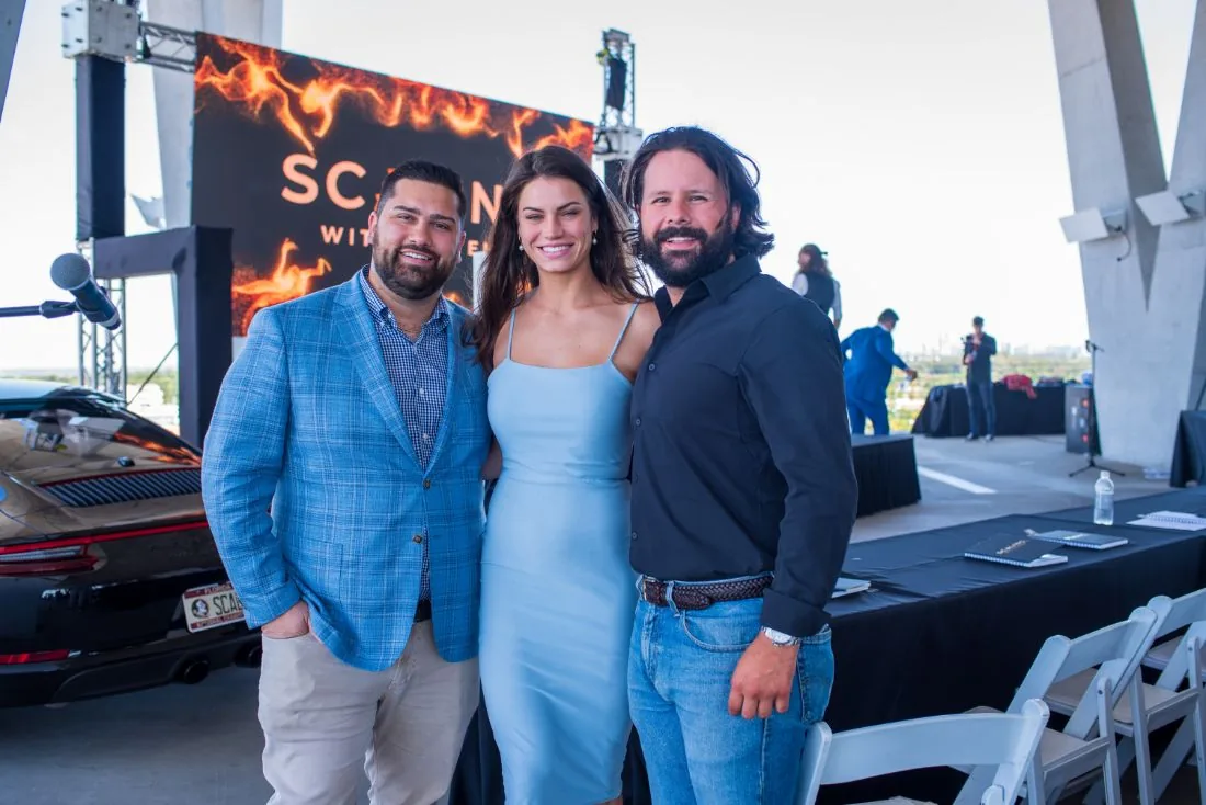 Three guests posing in front of the Scaling With Systems stage screen at Scaling With Systems LIVE in Miami