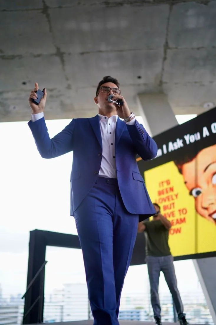 Speaker with a microphone on stage above the Miami skyline at Scaling With Systems LIVE in Miami