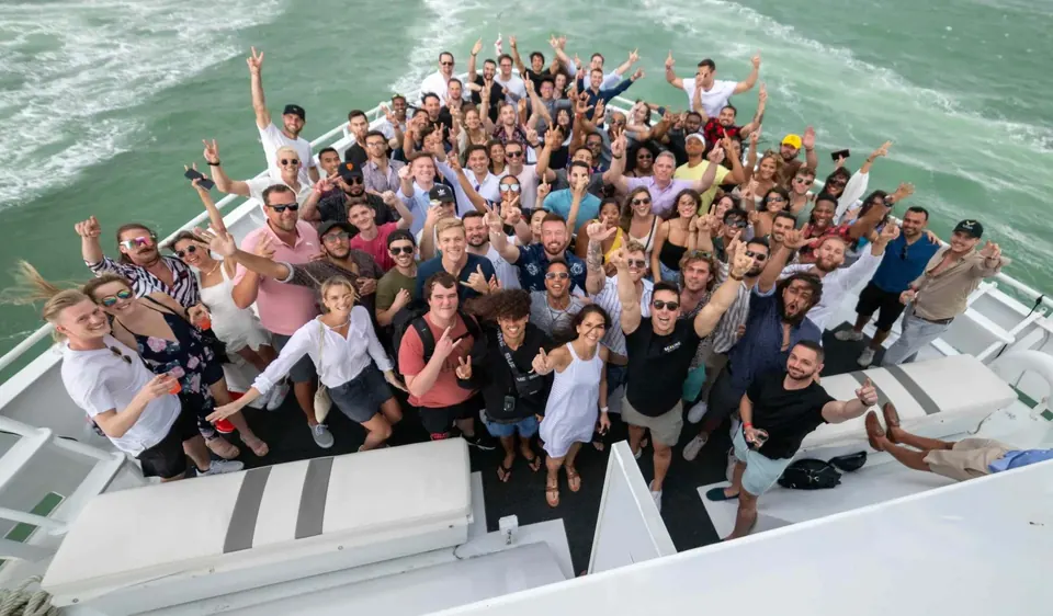 Attendees packed onto the bow of a yacht on the water, arms raised for the group photo, during Scaling With Systems LIVE in Miami